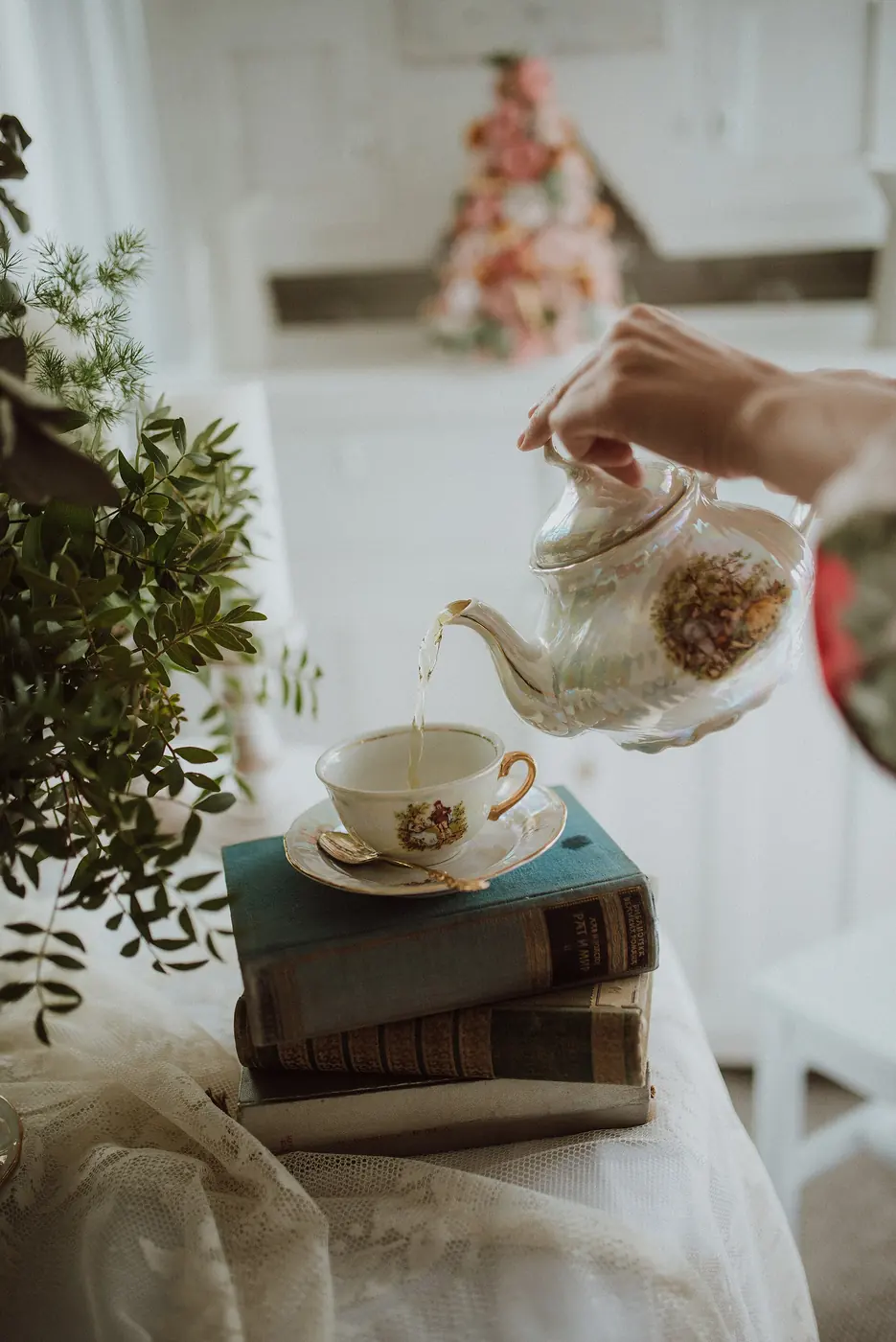 Tea being poured from a floral china teapot into a cup resting on old books