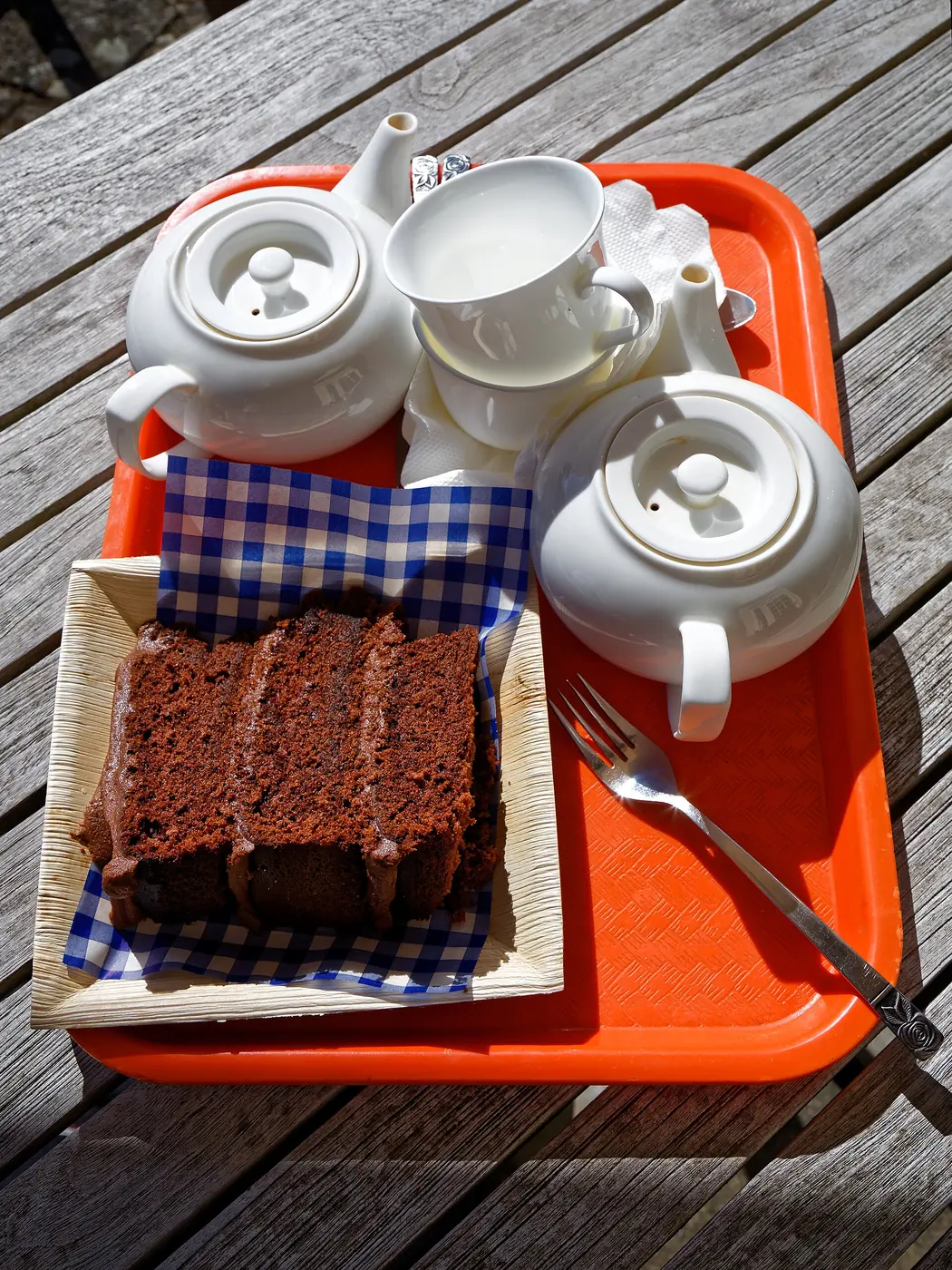 A tray with white teapots, cups and a slice of chocolate cake on a gingham napkin