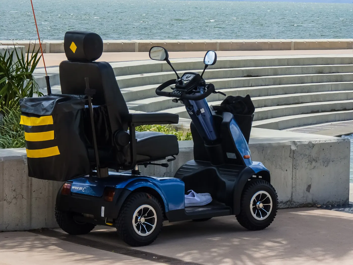 A blue mobility scooter parked beside steps on a seafront